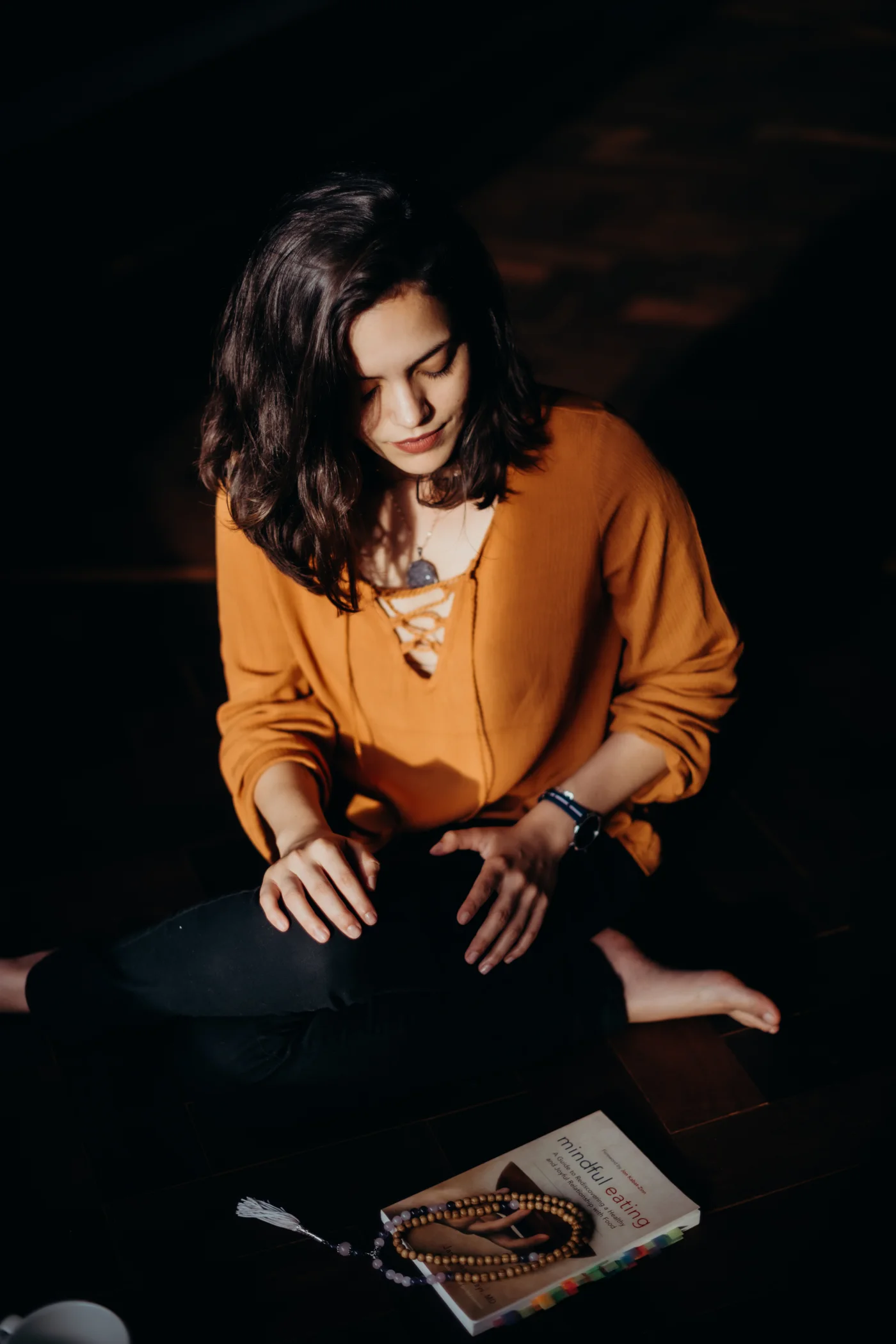 Driele Quinhoneiro sentada em postura meditativa, com o livro Mindful Eating de Jan Chozen Bays e um japamala à sua frente